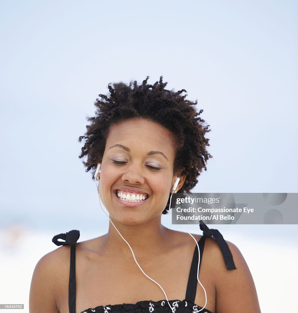 Young woman wearing earphones on beach, smiling with eyes shut