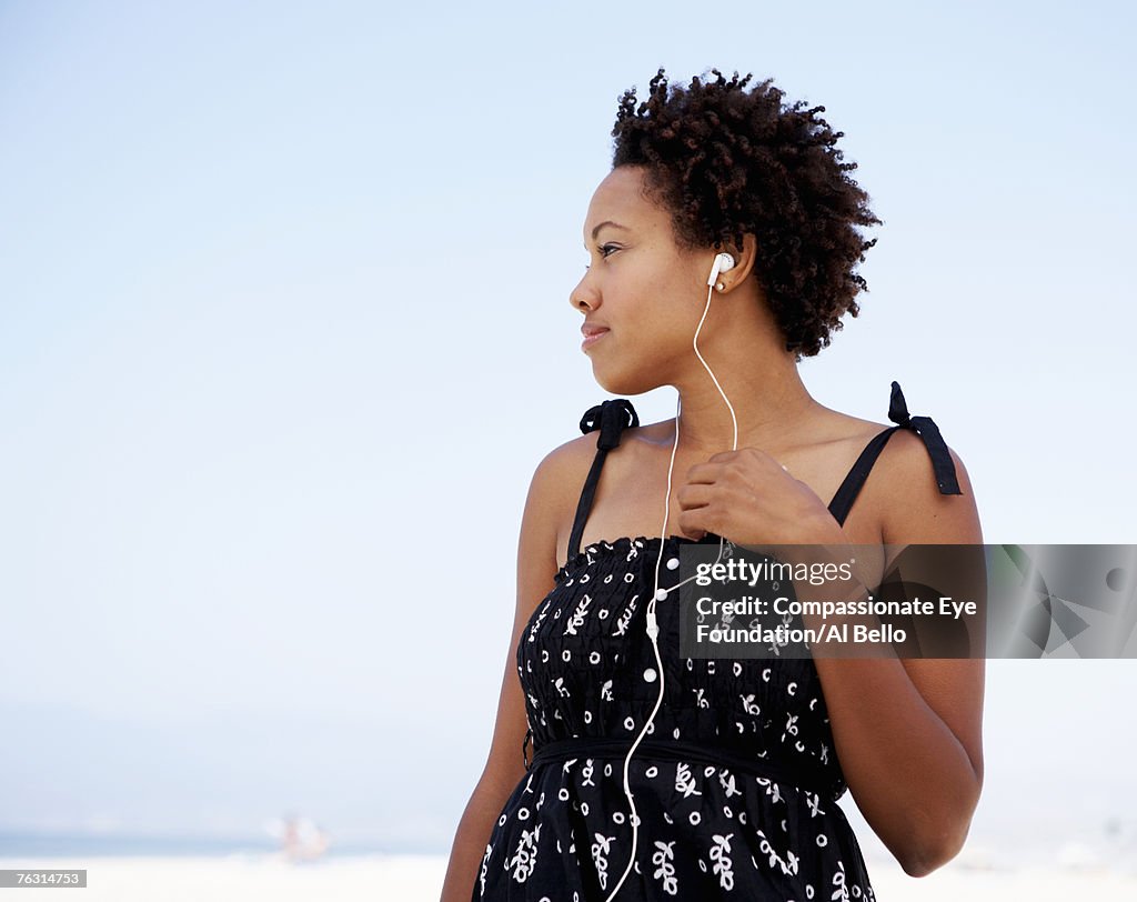 Young woman wearing earphones on beach, upper half