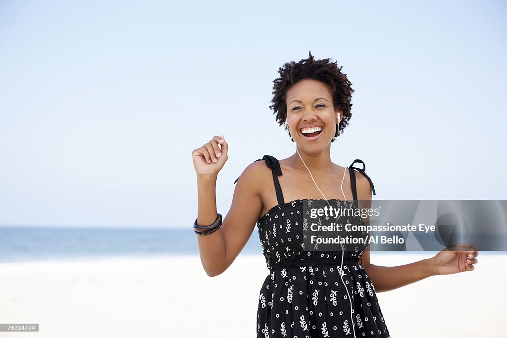 Young woman wearing earphones on beach, laughing, portrait, waist up