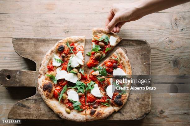 woman taking pizza slice from pizza on chopping board, overhead view - pizza slice stock pictures, royalty-free photos & images