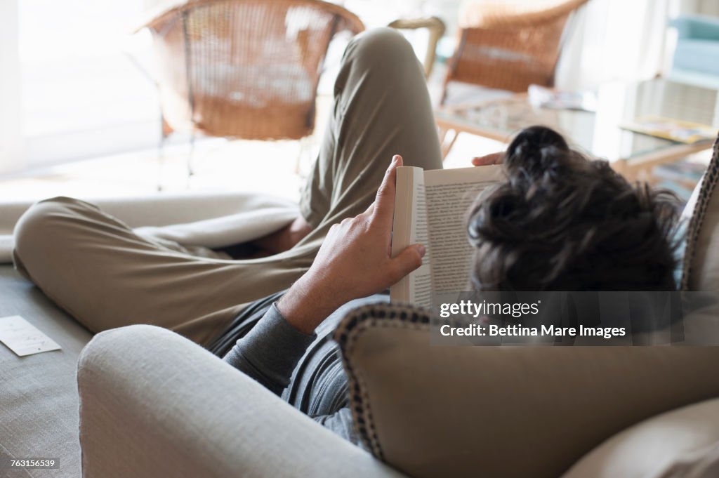 Mid adult man relaxing on sofa, reading book, rear view