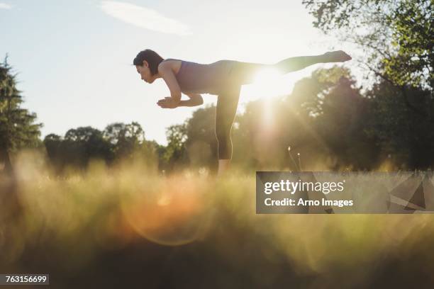 mature woman in park, balancing on one leg, in yoga position, low angle view - yoga outdoor stock pictures, royalty-free photos & images