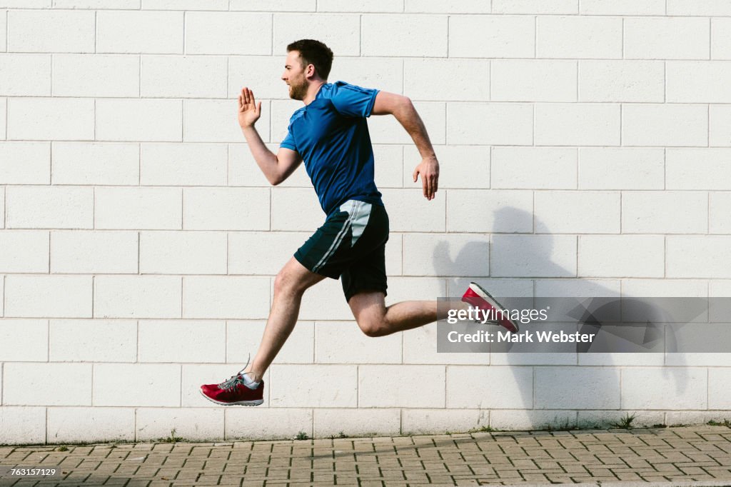Young male runner speed running along sidewalk