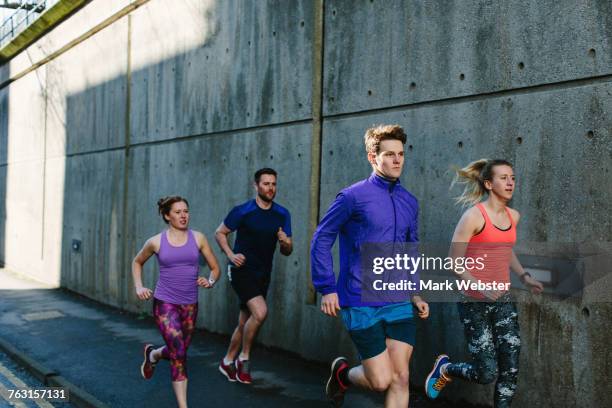 four young adult runners running along city sidewalk - live at leeds 2016 stock pictures, royalty-free photos & images
