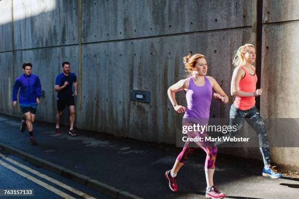 four young adult runners running along city sidewalk - live at leeds 2016 stock pictures, royalty-free photos & images