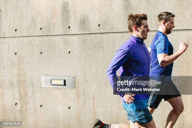 two young male runners running along city sidewalk - live at leeds 2016 stock pictures, royalty-free photos & images