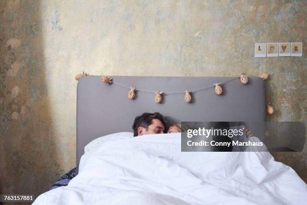 couple in bed, under the covers, kissing - man and woman kissing in bed stock pictures, royalty-free photos & images