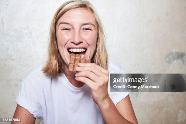 portrait of woman eating bar of chocolate - biting into chocolate stock-fotos und bilder