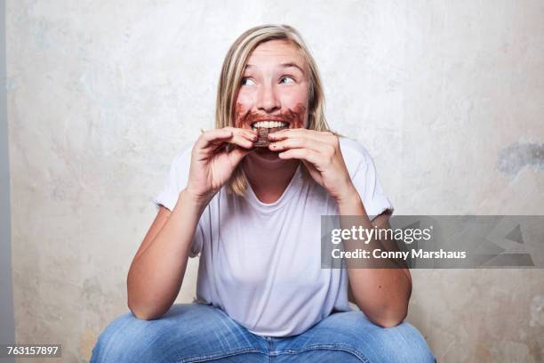 portrait of woman eating bar of chocolate, chocolate around mouth - chocolate face stock pictures, royalty-free photos & images