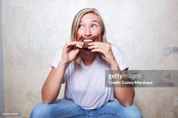 portrait of woman eating bar of chocolate, chocolate around mouth - chocolate face imagens e fotografias de stock