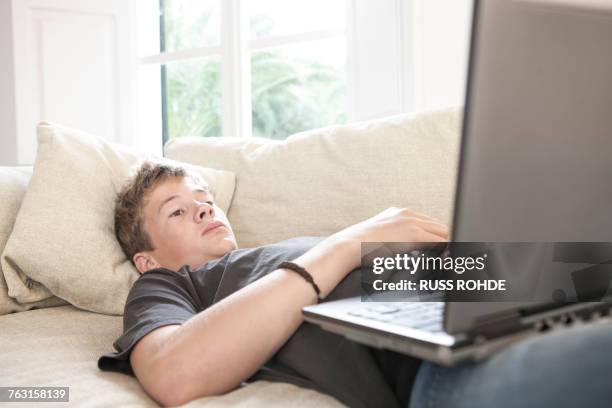 teenage boy lying on sofa looking at laptop - laziness stock pictures, royalty-free photos & images
