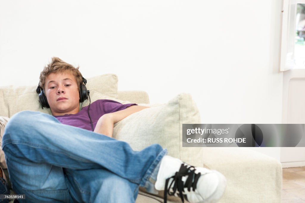 Teenage boy sitting on sofa listening to headphone music