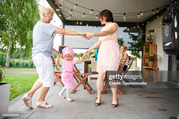 senior and mature women dancing with female toddler at family lunch on patio - great grandmother imagens e fotografias de stock