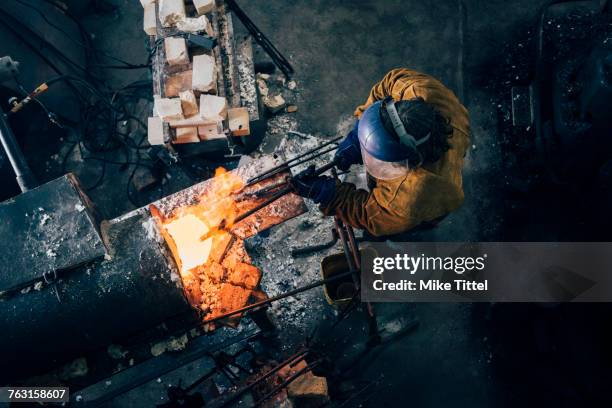 overhead view of blacksmith shaping red hot metal rod in workshop furnace - schmied stock-fotos und bilder