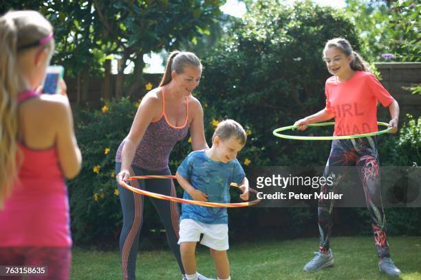 girl photographing mother and siblings hoola hooping in garden - girls in leggings stock-fotos und bilder