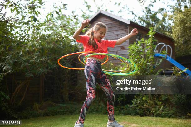 teenage girl hula hooping with four plastic hoops in garden - girls in leggings stockfoto's en -beelden