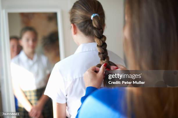 over shoulder view of mother plaiting teenage schoolgirl daughters hair - woman rear view mirror stock pictures, royalty-free photos & images