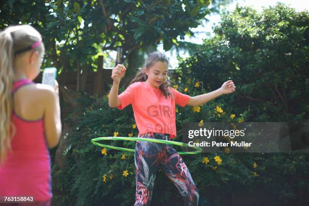 Girl photographing teenage sister hoola hooping in garden