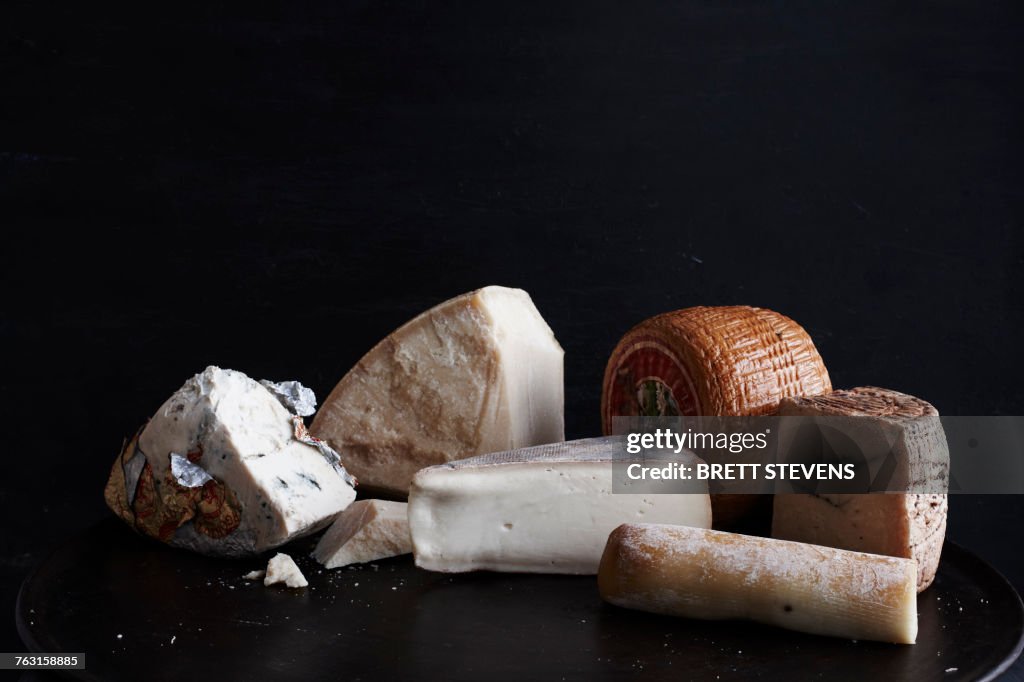 Selection of cheese on black plate against black background, close-up
