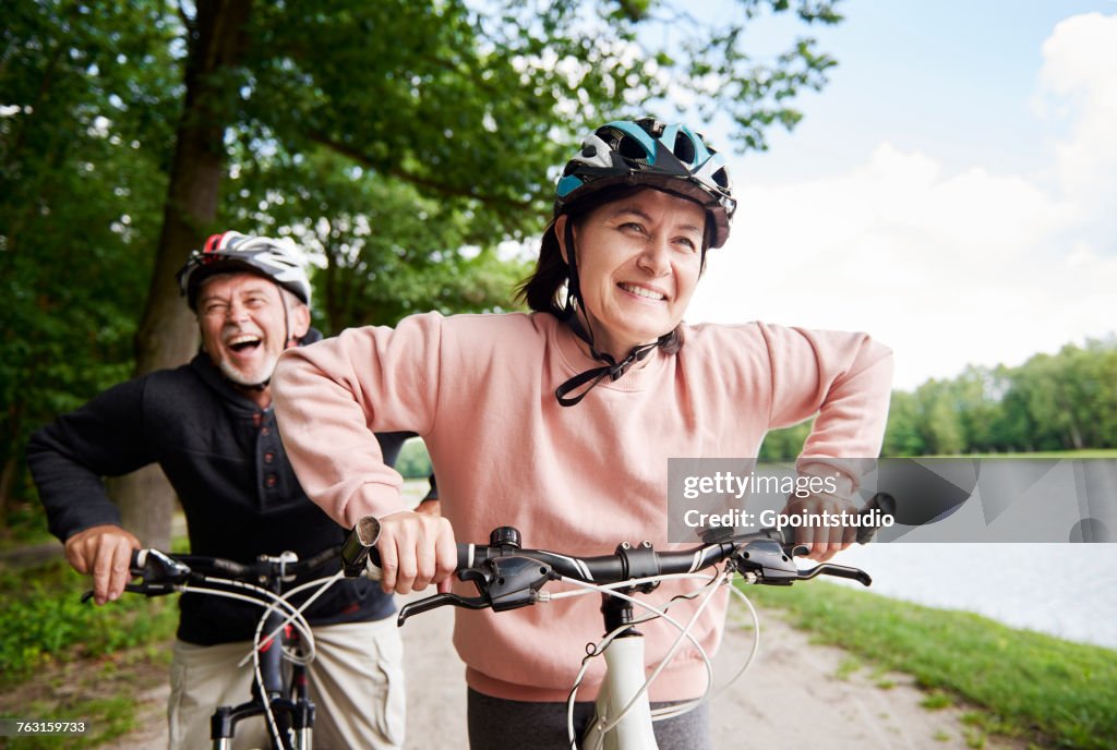 Mature couple cycling beside lake, laughing