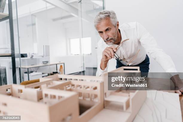 mature businessman examining architectural model in office - architectural model stockfoto's en -beelden