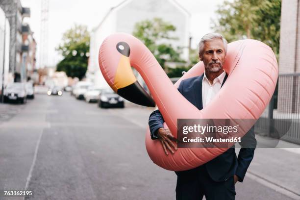 mature businessman on the street with inflatable flamingo - eccentrico foto e immagini stock