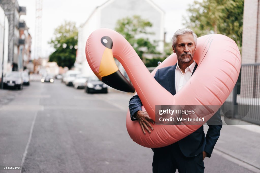 Mature businessman on the street with inflatable flamingo