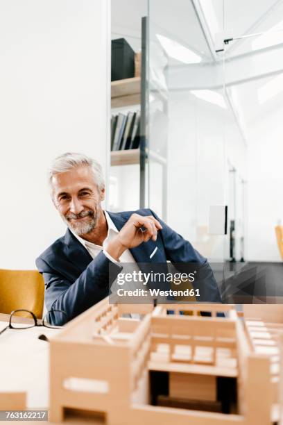 portrait of smiling mature businessman with architectural model in office - architekturmodell stock-fotos und bilder