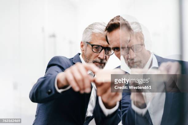two businessmen examining architectural model at glass pane - scrutiny foto e immagini stock