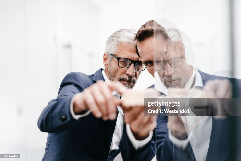Two businessmen examining architectural model at glass pane