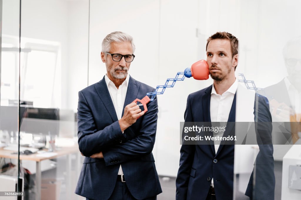 Mature businessman in office hitting colleague with boxing toy