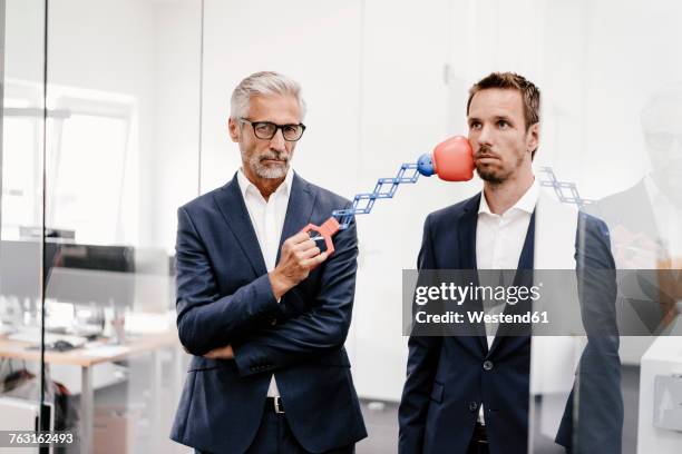 mature businessman in office hitting colleague with boxing toy - leadership fist ストックフォトと画像