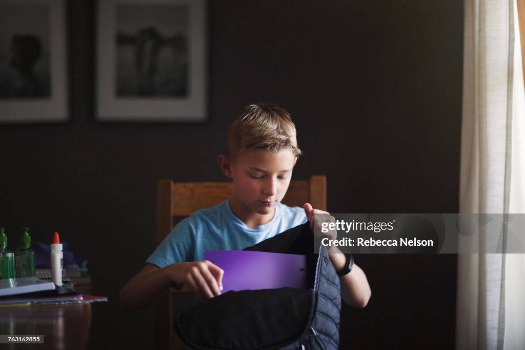 Boy packing backpack with school stationery supplies