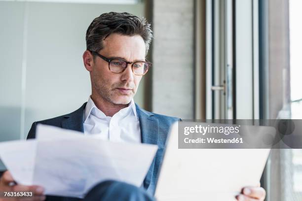 portrait of serious businessman with documents looking at tablet - reading document stock pictures, royalty-free photos & images