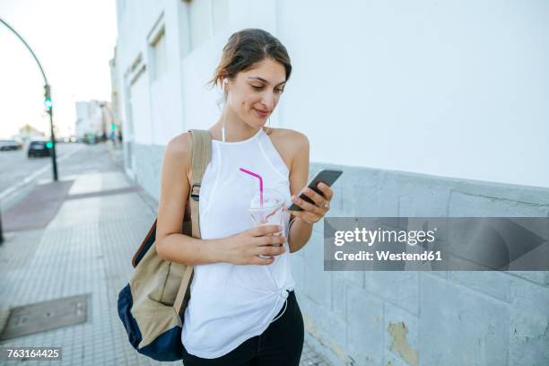young woman with cell phone and smoothie walking down the street - one young woman only foto e immagini stock