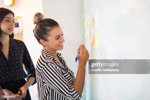 young businesswoman writing on whiteboard adhesive notes - meeting schreiben stock-fotos und bilder