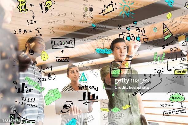 young businesswoman drawing diagrams on glass wall in creative office - heshphoto - fotografias e filmes do acervo