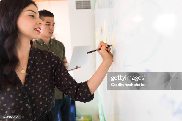 young businesswoman writing on whiteboard adhesive notes - heshphoto stock pictures, royalty-free photos & images