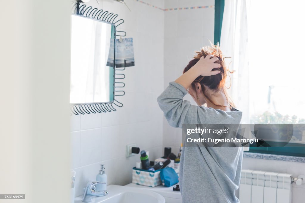 Young woman styling hair up at bathroom mirror