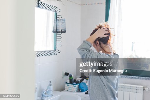 Young woman styling hair up at bathroom mirror Young woman styling hair up at bathroom mirror