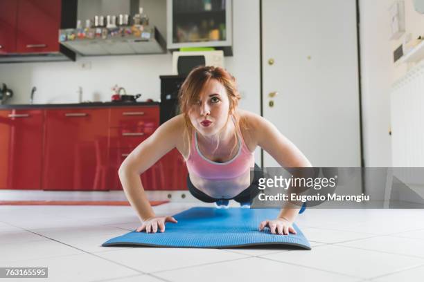 portrait of young woman doing push ups on kitchen floor - push ups stock pictures, royalty-free photos & images