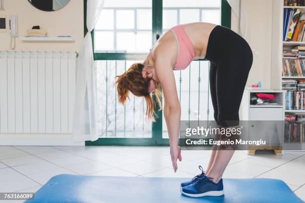 young woman practicing yoga bending forward on yoga mat - bending over stock pictures, royalty-free photos & images