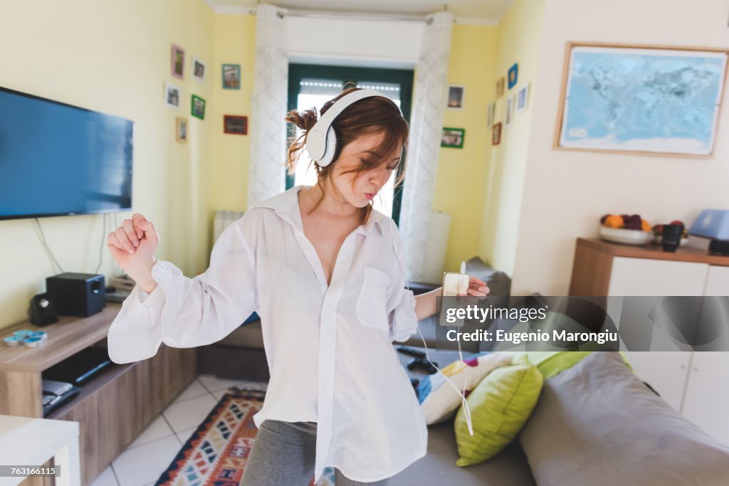 Young woman in sitting room dancing to smartphone music on headphones