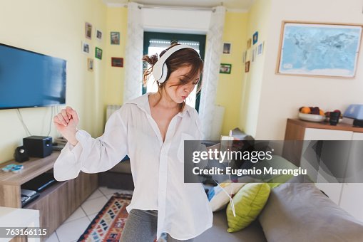 Young woman in sitting room dancing to smartphone music on headphones Young woman in sitting room dancing to smartphone music on headphones