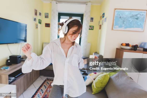 Young woman in sitting room dancing to smartphone music on headphones