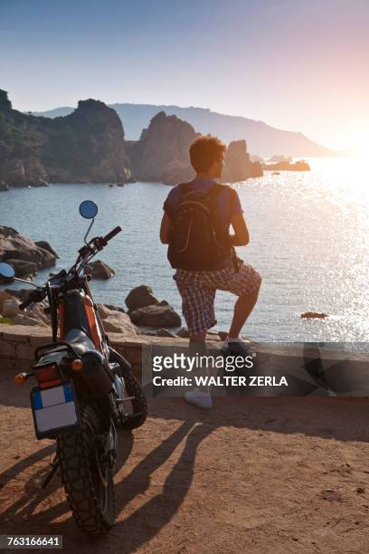 man with motorbike looking away at view of sunset over sea, olbia, sardinia, italy - mare moto foto e immagini stock