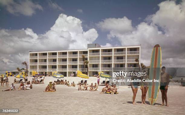 Posed portrait of groups of people as they sit or stand on the beach in front of the Thunderbird Motel, Myrtle Beach, South Carolina, 1960s.