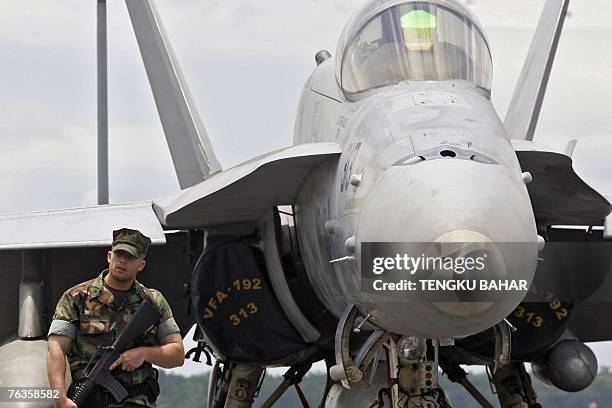 Navy sailor on sentry duty stands guard next to an F/A-18C Hornet strike aircraft on board the aircraft carrier USS Kitty Hawk during a port call in...