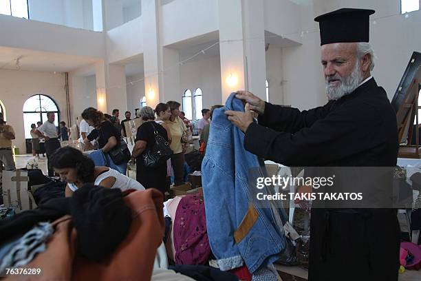 Priest selects clothes offered by the Greek Orthodox church inside the Agios Panteleimon church as part of aid to help the victims of fire disaster...