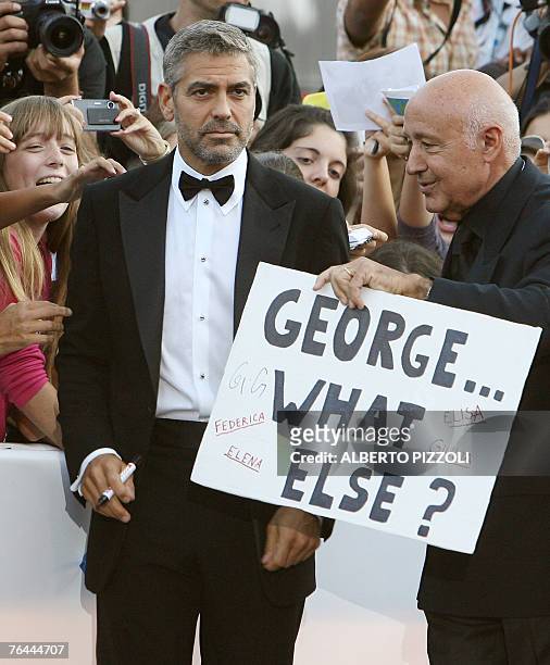Actor George Clooney is presented onto the red carpet by an unidentified usher holding a sign, on arrival for the screening of his movie "Michael...